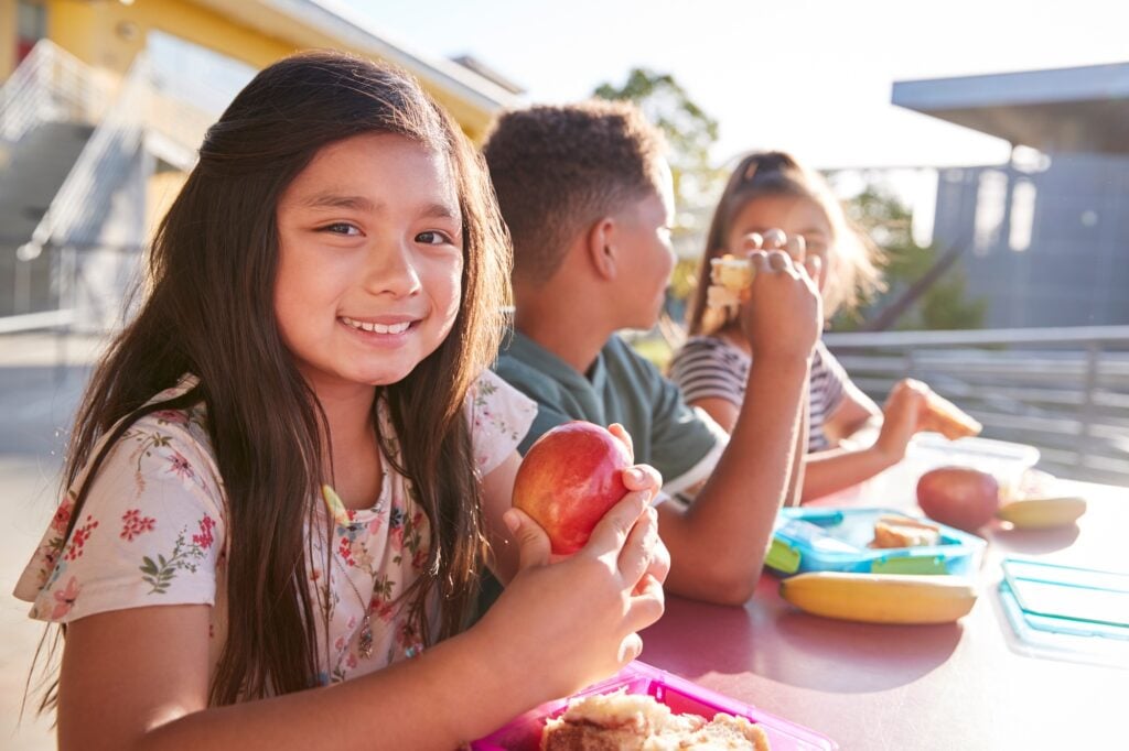 Girl at elementary school lunch table smiling to camera