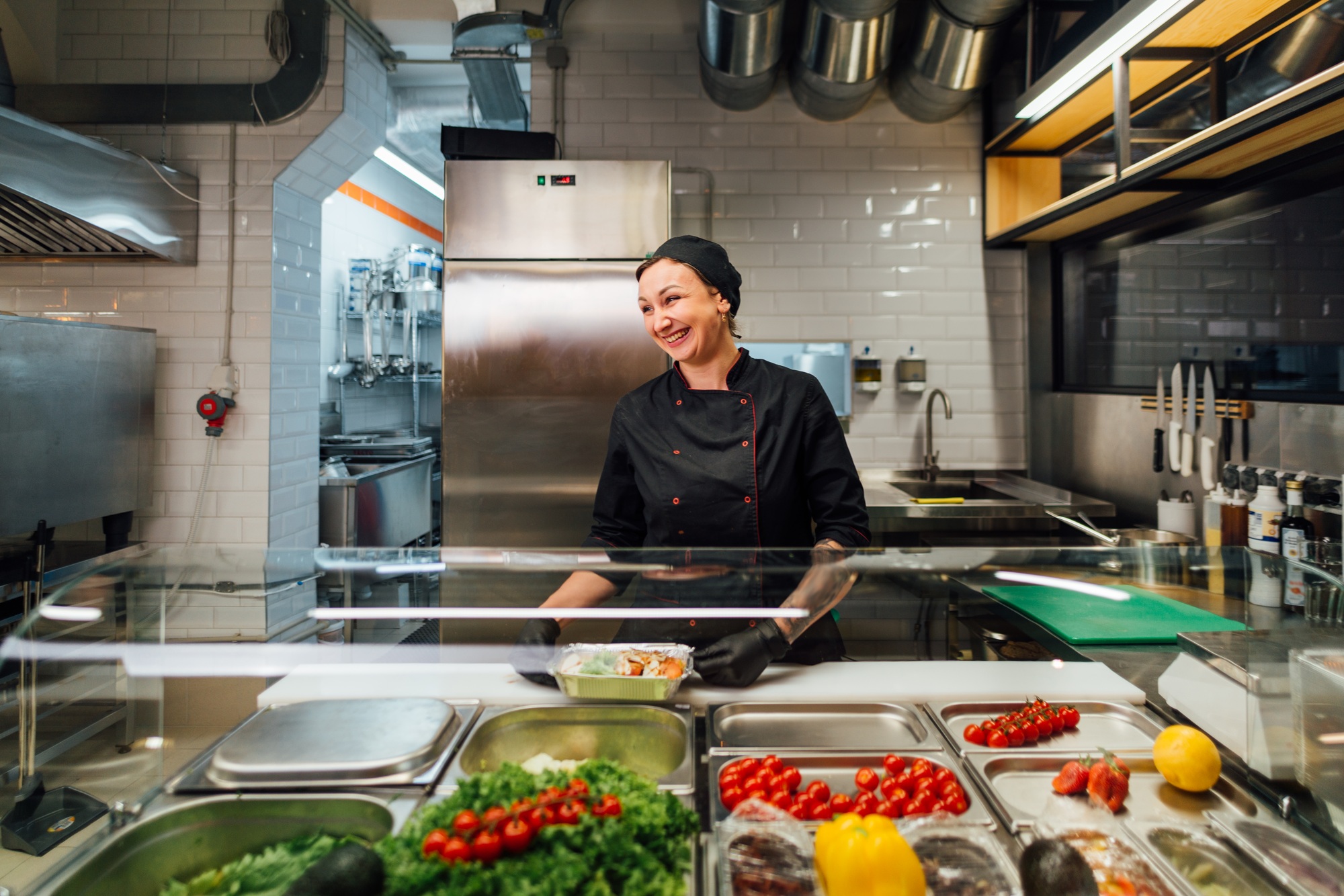 Joyful cafe worker prepares salad. Catering kitchen work.